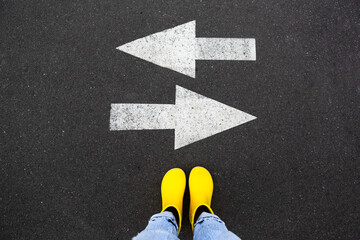 Yellow rubber boots on the asphalt road with drawn arrows pointing to two directions. Making...
