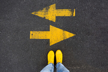 Yellow sneakers on the asphalt road with drawn arrows pointing to two directions. Making decisions...