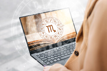 Astrological forecast for the zodiac sign scorpio. Woman holding an open laptop with a picture of a book and the zodiac circle