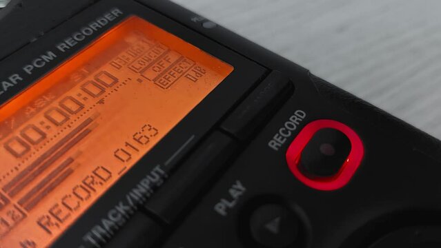 Finger presses record button of digital audio voice dictophone during interview or interrogation. Screen with wave form of speech recording of journalist. Electronic portable device for media reporter