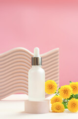 Obraz na płótnie Canvas Essential oil or serum and yellow chrysanthemum flowers on a beige podium. White matte bottle with pipette.