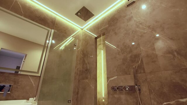 Modern bathroom interior ceiling with yellow led strip, porcelain stoneware tiles on the walls. Toilet, towel and washing machine. Stylish design, background