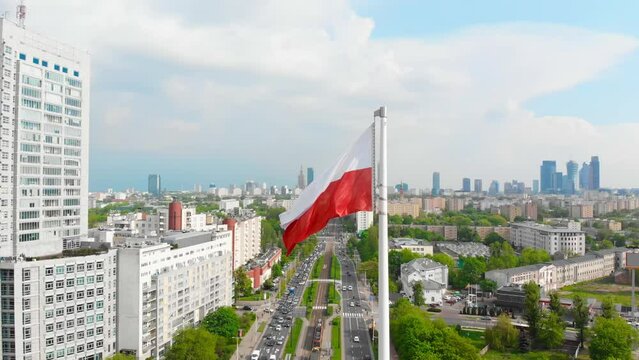 The white and red Polish flag waving in the wind. Warsaw city center in the background. Concept of national pride and celebration of the national day. Aerial view of the flag.
