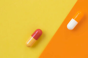 Two multi-colored capsules of the drug on a bright yellow-orange background, minimalism, macro.