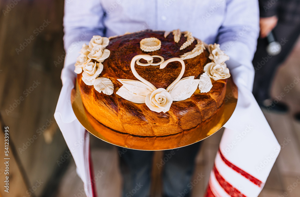 Wall mural A man, a father, holds a round loaf decorated with flowers, a swan with an embroidered towel in his hands. Wedding food photography.