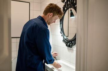 Man in dark-blue shirt in the bathroom washing hands - obrazy, fototapety, plakaty