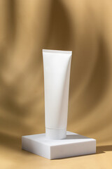 White cosmetic tube with no label on white podium on beige background with shadow