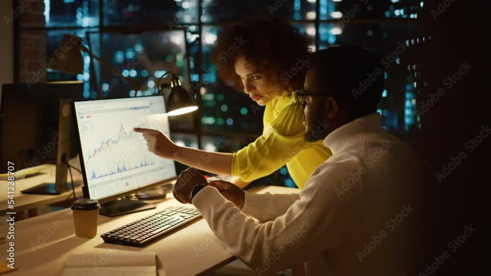 Aufkleber Team of Two Young Entrepreneurs Talking, Discussing Growth Strategy at a Desk with Computer. Stylish Businesspeople Work on an Investment and Marketing Report in a Creative Agency in the Evening.