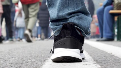 man legs on double white line close up and lot of people walking in middle of road street.city day festival urban national day barbeque street food.person's legs feet in different directions.road mark