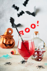 Halloween bloody cocktails. Two bloody cocktails glass goblets for Halloween and bottle form skull on light backgrounds. Decor concept for Halloween party with candy eyes, bats, spiders and pumpkins.