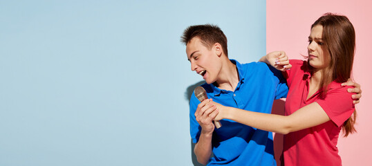 Portrait of young people, man and woman posing with microphone, singing battle isolated over blue-pink background. Flyer