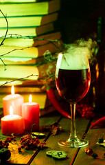 A glass of steaming wine on the table next to books and candles