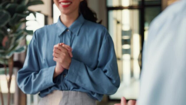 Multiracial group of young creative people in smart casual wear discussing business shaking hands together and smiling while standing in modern office. Partner cooperation, coworker teamwork concept.