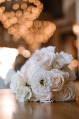 The wedding bouquet lies on a wooden table against the background of yellow bokeh circles. Modern bridal bouquet of roses and ranunculus.