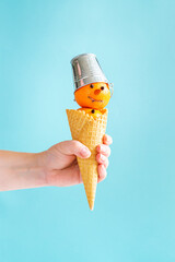 The hand is holding a waffle cone with a tangerine snowman..