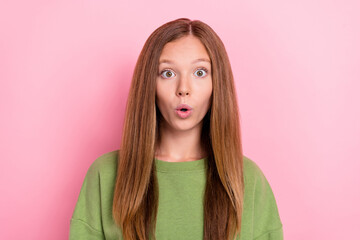 Portrait of impressed excited cute girl with long hairdo dressed green sweatshirt staring open mouth isolated on pink color background