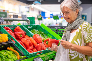 Senior woman selecting fresh vegetables holding a red peppers in the food department in supermarket...