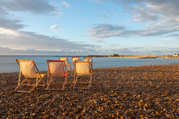 colourful deckchairs on the beach at Lyme Regis with The Cobb in the background in the early morning sunshine