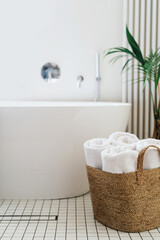Fototapeta na wymiar Fresh rolled towels in wicker basket close to white bathtub
