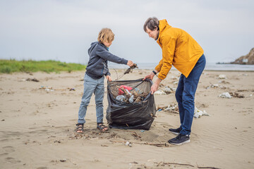 Dad and son in gloves cleaning up the beach pick up plastic bags that pollute sea. Natural...