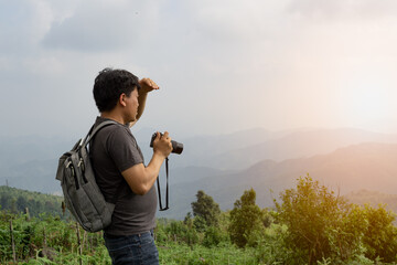 A sian man with his backpack and camera is travel alone and look at far a way, nature travel and environment concept, copy space for individual text