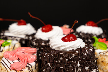Cakes with chocolate, cherries and cream on a black background.