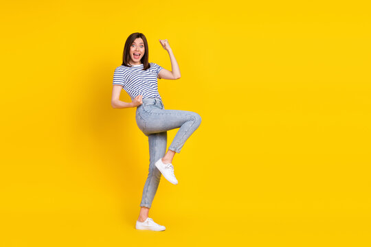 Photo of satisfied overjoyed lady raise arm leg rejoice yeap stand empty space isolated on yellow color background