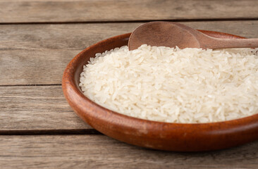 Narrow focus, raw white rice in a plate over wooden table with copy space