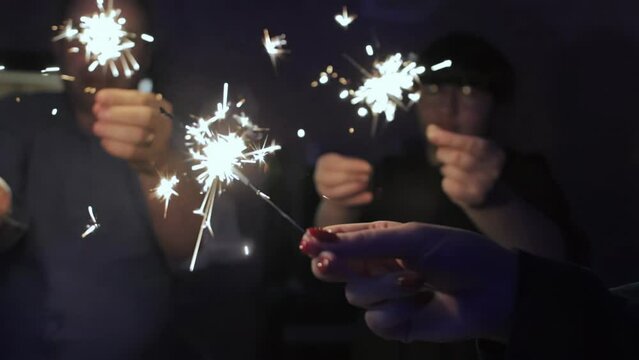 People hold sparklers in their hands that burn in dark at home festive table in hall without light. Christmas and New Year. Family celebration and fun. Bengal fire in slow motion