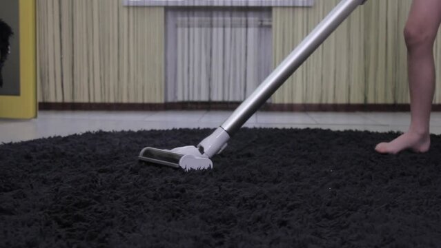Young guy vacuum cleaner cleans the black carpet in the room
