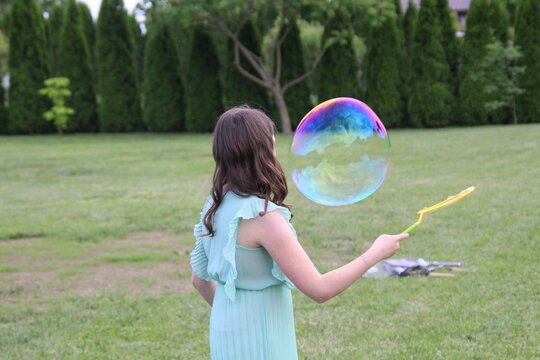 Female child holding a bubble wand playing with a bubble in a park