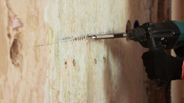 Wall chasing a groove in the wall for cable routing.  2 Shots. A worker using a perforator and a chisel strobes a wall for laying an electric cable. Mid shot and close-up.