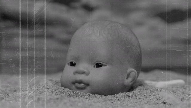 A baby doll head buried in sand on beach 