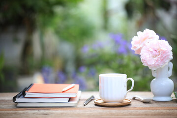 pink rose in a jar and notebook and coffee white cup on wooden table