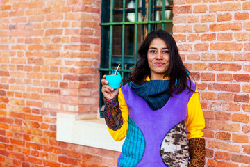  Smiling latin american girl drinking mate with colorful hoodie
