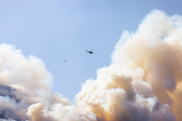 Wildfire Service Helicopter flying over BC Forest Fire and Smoke on the mountain near Hope during a hot sunny summer day. British Columbia, Canada. Natural Disaster