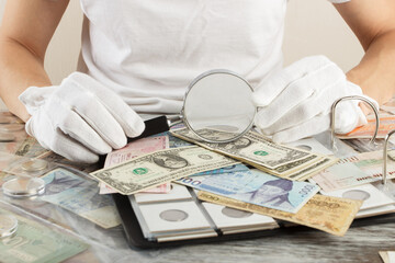 Hands with different old collector's coins and banknotes with magnifying glass
