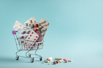 Many medicine pills, tablets and vitamins in a small supermarket shopping cart on a blue  background, pharmaceutical picture taken with soft focus Pharmacy theme, capsular tablets   © Лариса Василенко