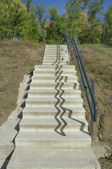 Stone stairs in the park with iron railings and shadow. Landscaping of the park area with trees against the blue sky. Park landscape.