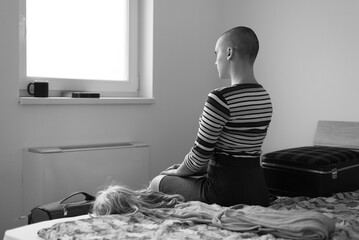 Sick bald woman cancer patient sitting on hospital bed before going home in black and white