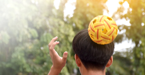 Young southeast asian male sepak takraw player using his right hand  to hold ball on his head, outdoor sepak takraw playing after school, soft and selective focus on ball.