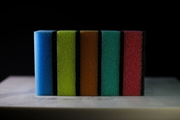 kitchen sponges of different bright colors for washing surfaces lie on a marble kitchen cutting board on a dark background. for advertising banners labels