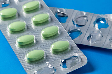Closeup green pills in blister pack on blue background. Use of medications and drugs. Medical and healthcare concept, pharmaceutical industry - obrazy, fototapety, plakaty