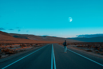 silhouette of a person walking on the road in the desert looking at the moon at sunset