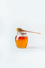close-up on a jar of honey and a wooden spindle for honey on a white background