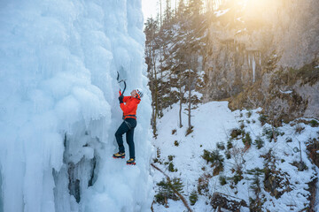Alpinist man with ice climbing equipment on a frozen waterfall