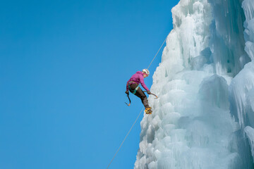 Alpinist woman with ice climbing equipment on a frozen waterfall