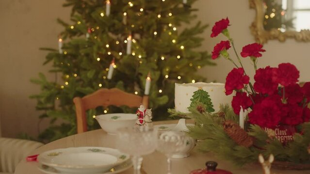 Christmas Decorated Table at Home with flowers and Christmas cake. Christmas Tree on background. Celebrating interior for New Year Party at Home. Family Dinner. Marry Christmas.