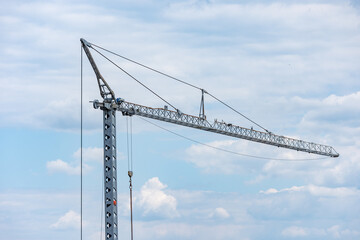 Gray steel construction crane with hooks against a sky with clouds