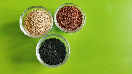 Spices and seeds displayed in separate glass bowls against a pretty green background.